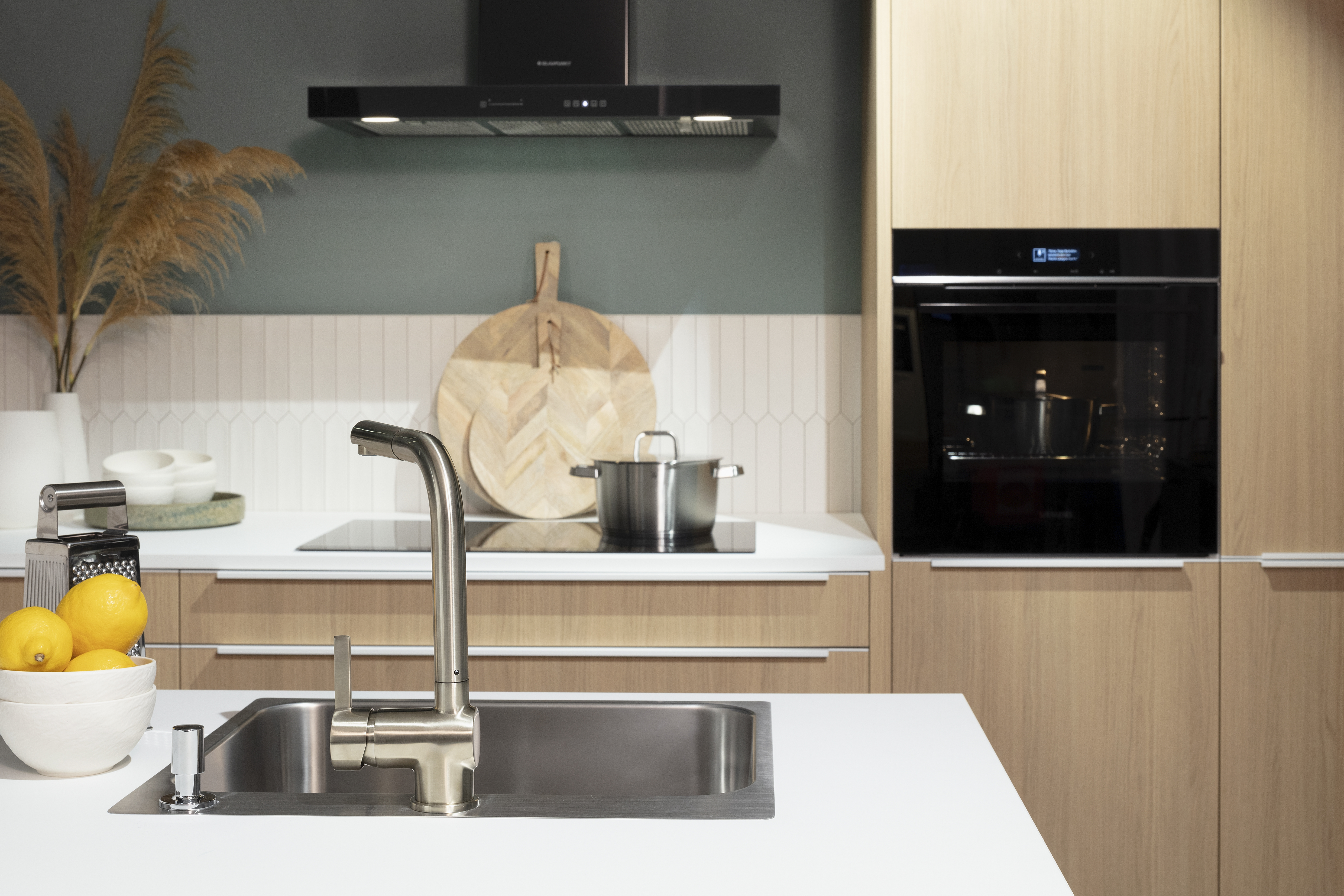 Häcker-Küche in Montreal Eiche-Natur-Repro Spüle im Vordergrund und Kochfeld mit Dunstabzug im Hintergrund.